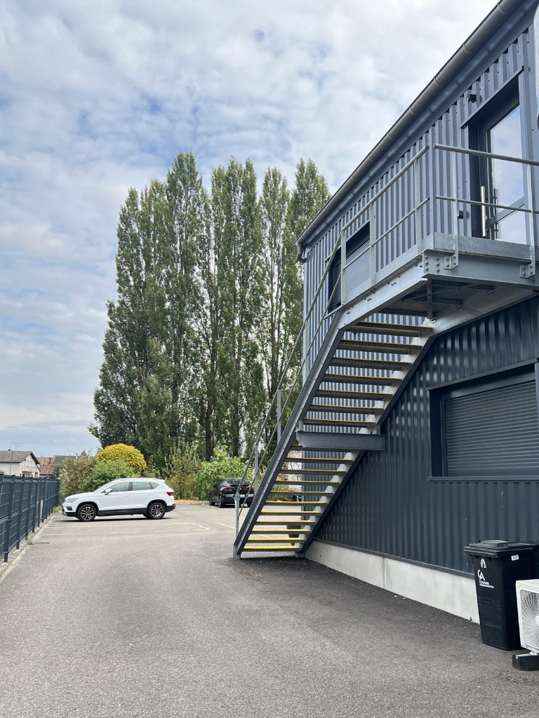 Vue du stationnement, du bâtiment et de l’escalier extérieur.